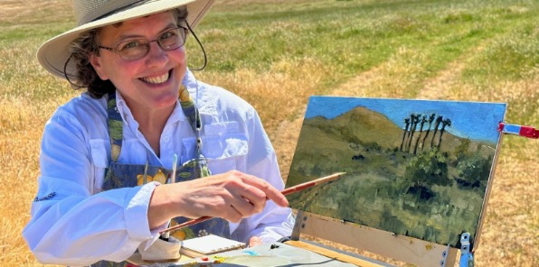Artist with paining in front of golden rolling hills. 