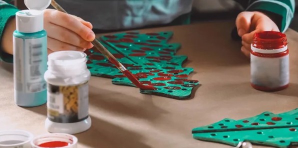 Child paints green Christmas Tree ornament with red paint 