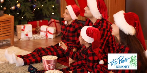 Family dressed in matching Chrostmas pajamas and Santa hats watching a holiday movie.