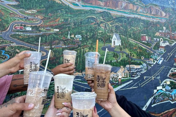 coffee drinks held in hands in front of the mural art of Oakhurst, Ca